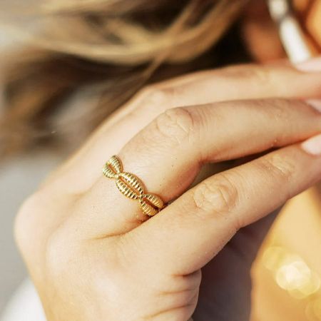 Close-up van een gouden gedraaide cowrie-schelp ring uit de set, gedragen op een vinger.