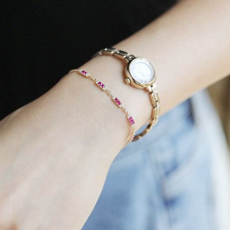 Pulsera de eslabones de charm de plata esterlina 925 con rubí para mujeres (Juego de 5) - Una elegante pulsera de charm de plata esterlina 925 con un rubí rosa, llevada con estilo en una muñeca junto a un reloj de oro, mostrando su diseño versátil.