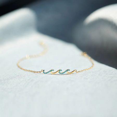 Vista detallada de la pulsera Glittering Waves chapada en oro, que presenta su motivo de ola y piedras de circonio azul.
