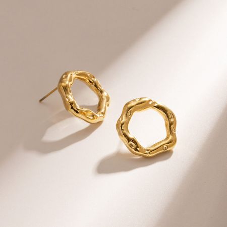 Un par de aretes de oro martillado con una forma circular irregular sobre un fondo blanco.