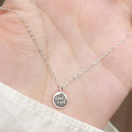 Le collier en argent 'Bonne Chance' tenu dans une main pour montrer son échelle et sa nature délicate.