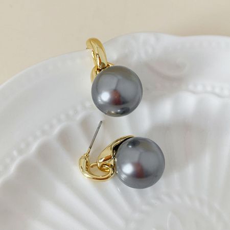 スタイリッシュなダークグレーのパールイヤリングが金のセッティングで貝皿に展示されています。