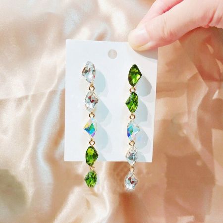 Prise de vue détaillée des pierres précieuses vertes et claires en forme de goutte sur les boucles d'oreilles pendantes plaquées or.