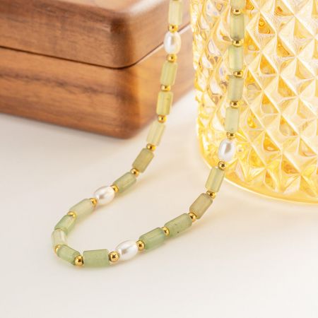 Un collar de cuentas verdes y perlas, elegantemente dispuesto con acentos dorados, mostrado con elementos decorativos.