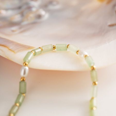 Una pulsera de cuentas verdes con un charm de oro, bellamente exhibida sobre una concha para evocar un ambiente playero y boho.