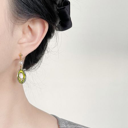 Close-up view of a gold-plated enamel earring with green floral details and a pearl drop.
