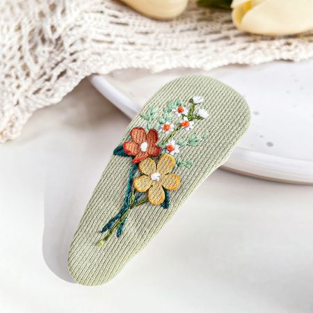 繊細な花柄刺繍が施された緑の布製ヘアクリップの詳細ショット。