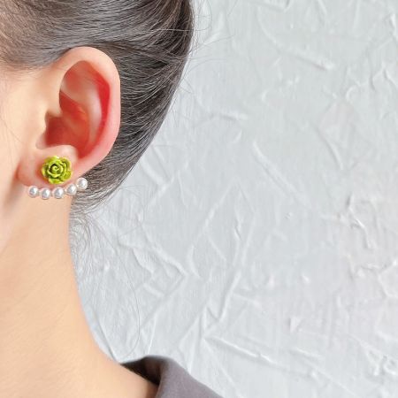 多用途の緑の花スタッドとパールフープイヤリングを着用しているモデル。