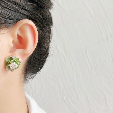緑のエナメル椿の花のパールスタッドイヤリングを披露するモデル。