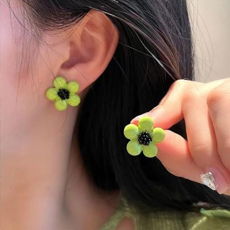 シンプルな背景にある鮮やかな緑のデイジー花のスタッドイヤリングのペア。