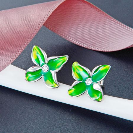 Primo piano degli orecchini a bottone a forma di fiore in smalto verde con dettagli in argento e una pietra centrale.