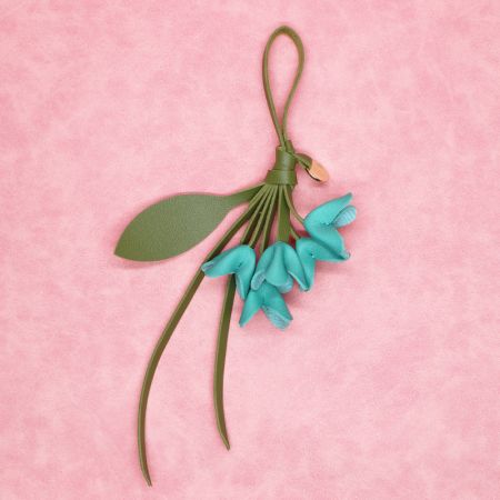 Porte-clés en cuir PU bleu canard en forme de fleur avec une sangle en cuir verte, présenté sur un fond rose.