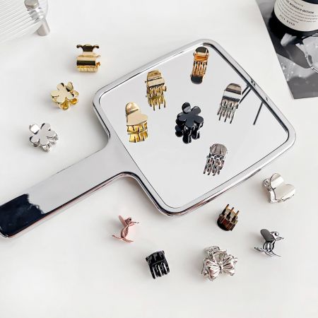 Various mini metal hair clips in gold, silver, and black displayed with their reflections.