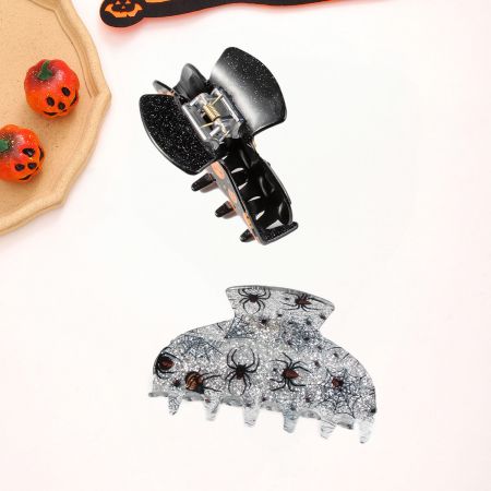 Eine schwarze, schleifenförmige Halloween-Klammer und eine klare Spinnennetzklammer.