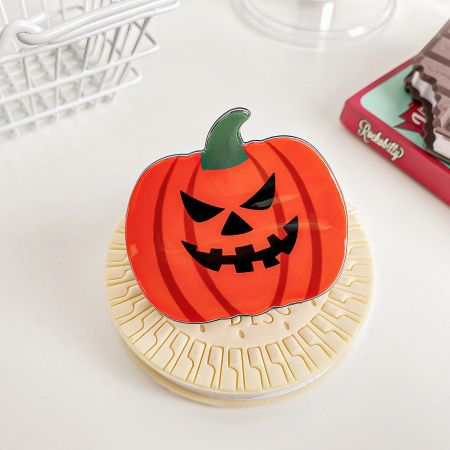 The jack-o'-lantern pumpkin hair clip displayed on a coaster, highlighting its vibrant orange color and cheerful expression.