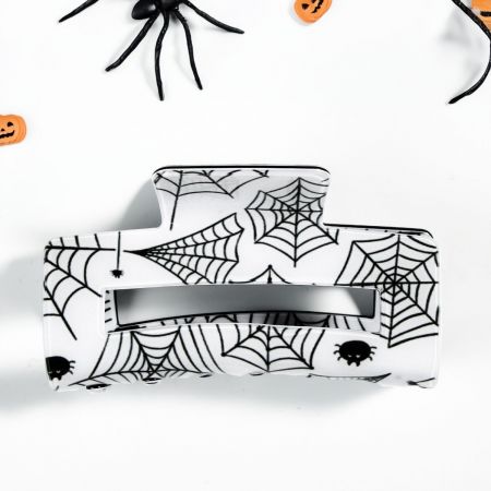 Een close-up van een zwarte haarclaw met spinnenwebpatroon, ideaal voor Halloween-haarstijlen.