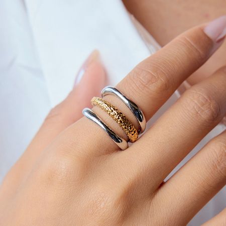 Model's hand met een stapel van drie bicolor roestvrijstalen ringen, die laat zien hoe ze samen gestyled kunnen worden.