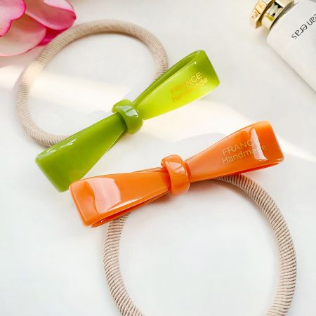 Twee handgemaakte haarbandjes, één groen en één oranje, met decoratieve strikken.