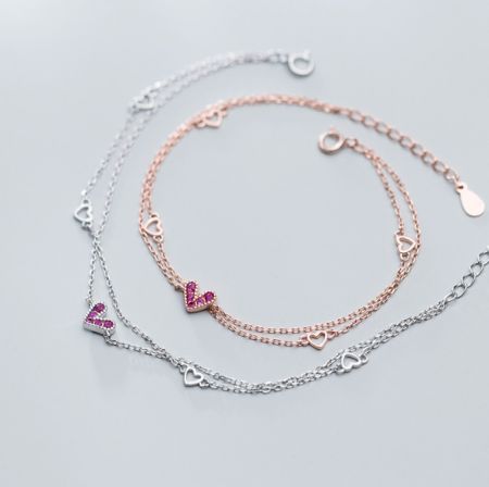 925 Sterling Zilveren Roze Hart Armband - Een paar hartarmbanden van 925 sterling zilver, één in roségoud met roze cubic zirconia en de andere in zilver met heldere edelstenen, elegant gepresenteerd.