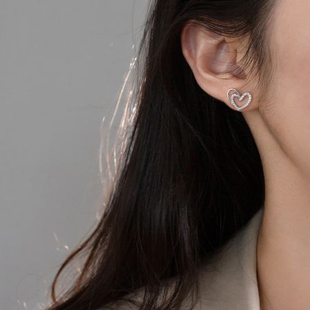 Close-up van een vrouw die de 925 zilveren holle hart stud oorbel draagt.