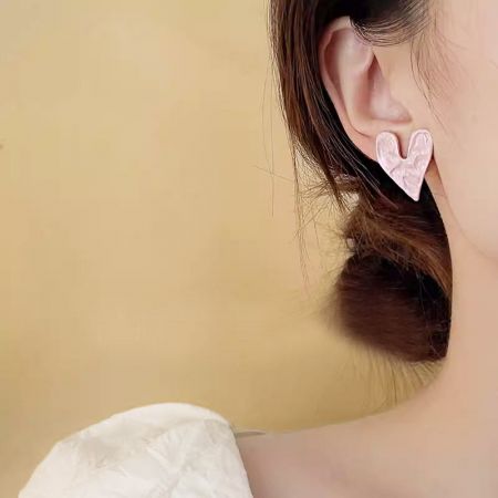 Detailed close-up of the pink heart stud earring on a model's ear.