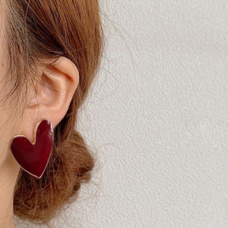 白いエナメルハート型スタッドピアスを着用した女性の詳細なビュー。