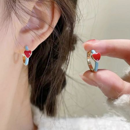 Vue en gros plan de la boucle d'oreille huggie en or et émail en forme de cœur portée.