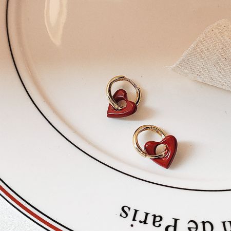 Close-up of the red and gold heart-shaped earrings on a white display plate.