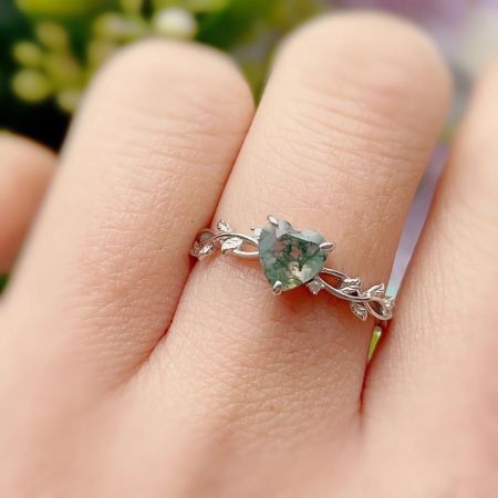 Close-up van de groene zircon hart ring gedragen op een vinger, met de nadruk op de ingewikkelde zilveren bladeren band.