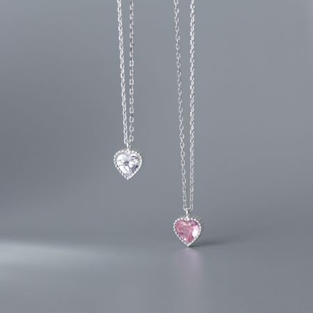 A pair of heart necklaces featuring clear and pink gemstones on silver chains.