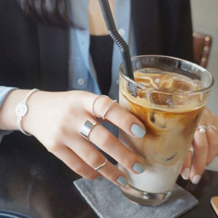 Image de style de vie d'une femme portant l'ensemble de bagues larges en argent 925 tout en tenant un café glacé, parfait pour la mode quotidienne.