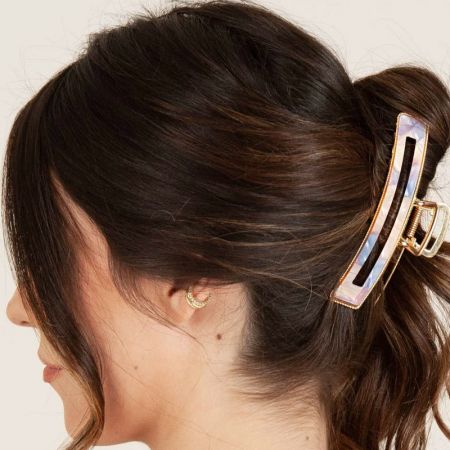 Una donna con i capelli raccolti in un chignon, acconciati con una clip per capelli in acetato iridescente con un accento dorato.