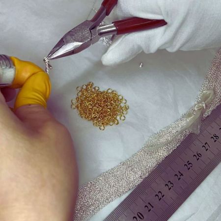 Primer plano de un joyero experto conectando eslabones de una delicada cadena, un paso clave en el ensamblaje de joyas.