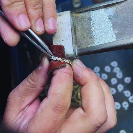Primer plano de un artesano colocando diamantes en una cadena de oro.