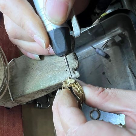 Primer plano del proceso de fabricación de joyas, mostrando un grabado detallado en un anillo de oro.