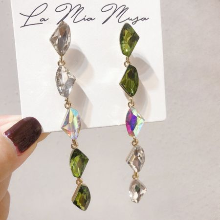 Vue rapprochée des longues boucles d'oreilles pendantes en strass avec des pierres précieuses claires et vertes sur une carte d'affichage.