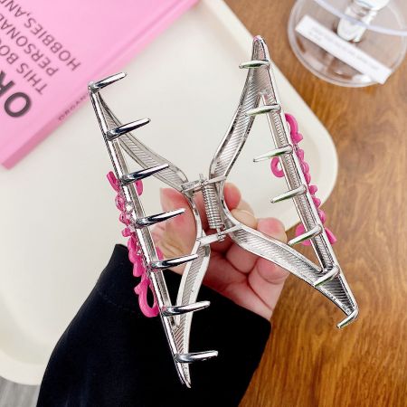 Clips de metal para el cabello en forma de garra con letras rosas al por mayor. - Un gran clip de metal en forma de mariposa plateada con acentos rosas, sostenido en la mano para mostrar su tamaño y detalle.