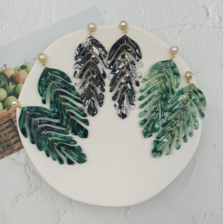 Boucles d'oreilles en acrylique en forme de feuille verte - Gros plan sur les boucles d'oreilles en acrylique en forme de feuille verte, mettant en valeur le design détaillé en résine verte et noire avec des accessoires en métal doré et une petite perle.