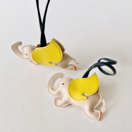 Dos charms de bolso en forma de elefante de cuero, uno blanco y uno gris, mostrando su detallada artesanía.