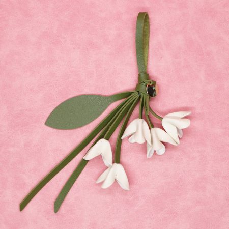 Gros plan d'un porte-clés en cuir PU blanc en forme de fleur avec une sangle en feuille verte sur un fond rose.