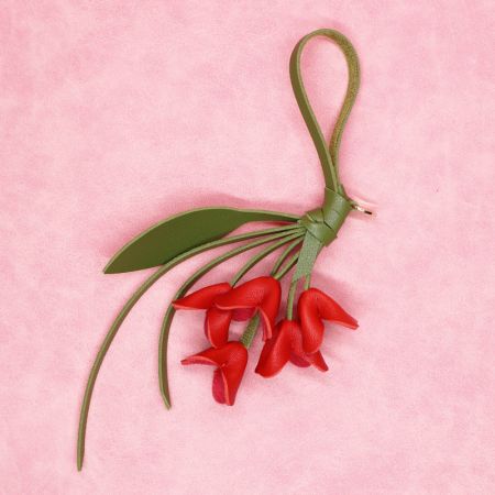 Porte-clés en cuir PU rouge vif en forme de fleur avec une sangle verte et un détail en feuille.