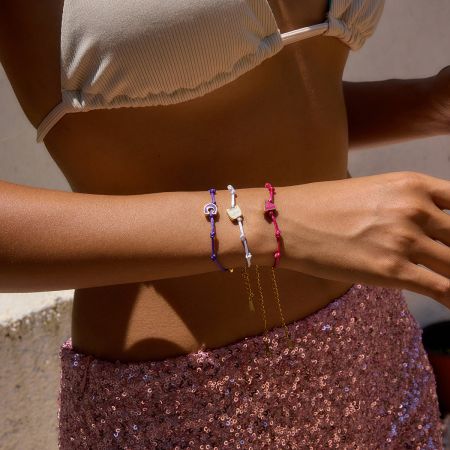 複数のゴールドプレートのイニシャルブレスレットを着用した女性のライフスタイルショットで、スタイリッシュで重ね着できるデザインを披露しています。