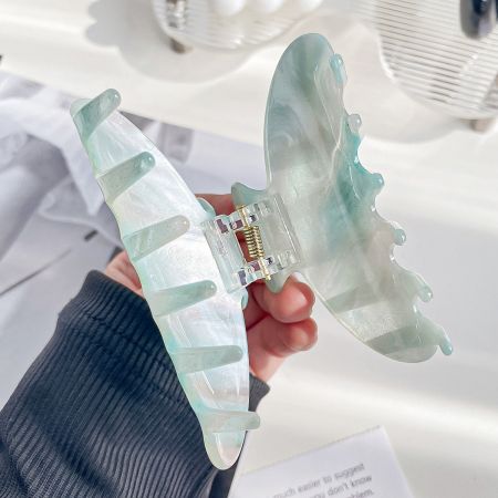 Close-up of a light blue-green butterfly-shaped acetate hair clip with gold details.