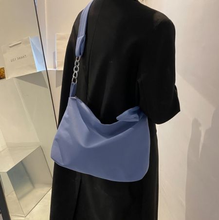 黒いドレスを着たモデルが、クロスボディスリングバッグのライトブルー版を披露し、そのサイズとスタイルを示しています。