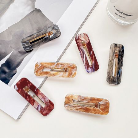 Lifestyle shot of colorful marbled hair clips arranged next to a lit scented candle.