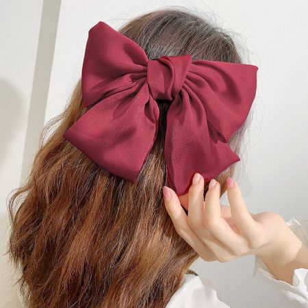 A woman wearing a large maroon fabric bow hair clip, showcasing its elegant style.