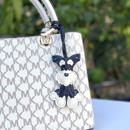 Le charme de chien Schnauzer attaché à un élégant sac à main Michael Kors, démontrant son utilisation comme accessoire de sac.