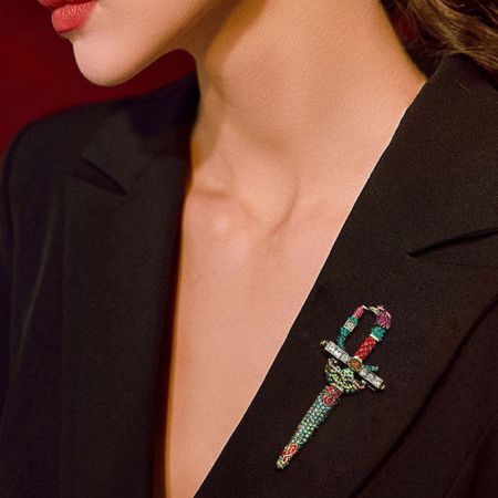 Broche de cristal retro de espada para trajes de hombre. - Un elegante broche de cristal retro de espada con strass y cuentas multicolores sujeto a la solapa de una chaqueta de traje negra, mostrando su diseño elegante y audaz.