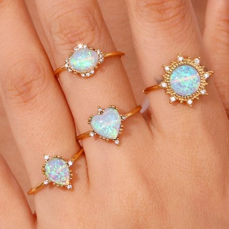 Close-up of four different opal ring designs: heart, oval, round, and teardrop shapes.