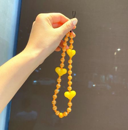 Ein detaillierter Schuss des lebhaften orangefarbenen Perlen-Handyriemens, der die zahlreichen Herzdekorationen hervorhebt.